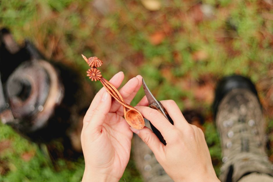 A person carves a wooden spoon outdoors, showcasing craftsmanship and nature.